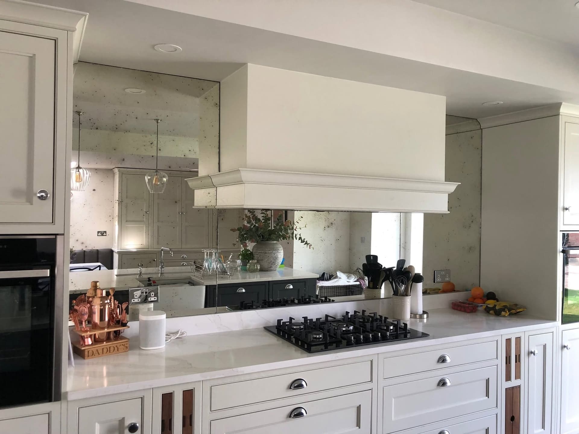 Antique mirror splashback behind a gas hob and canopy hood in a painted kitchen