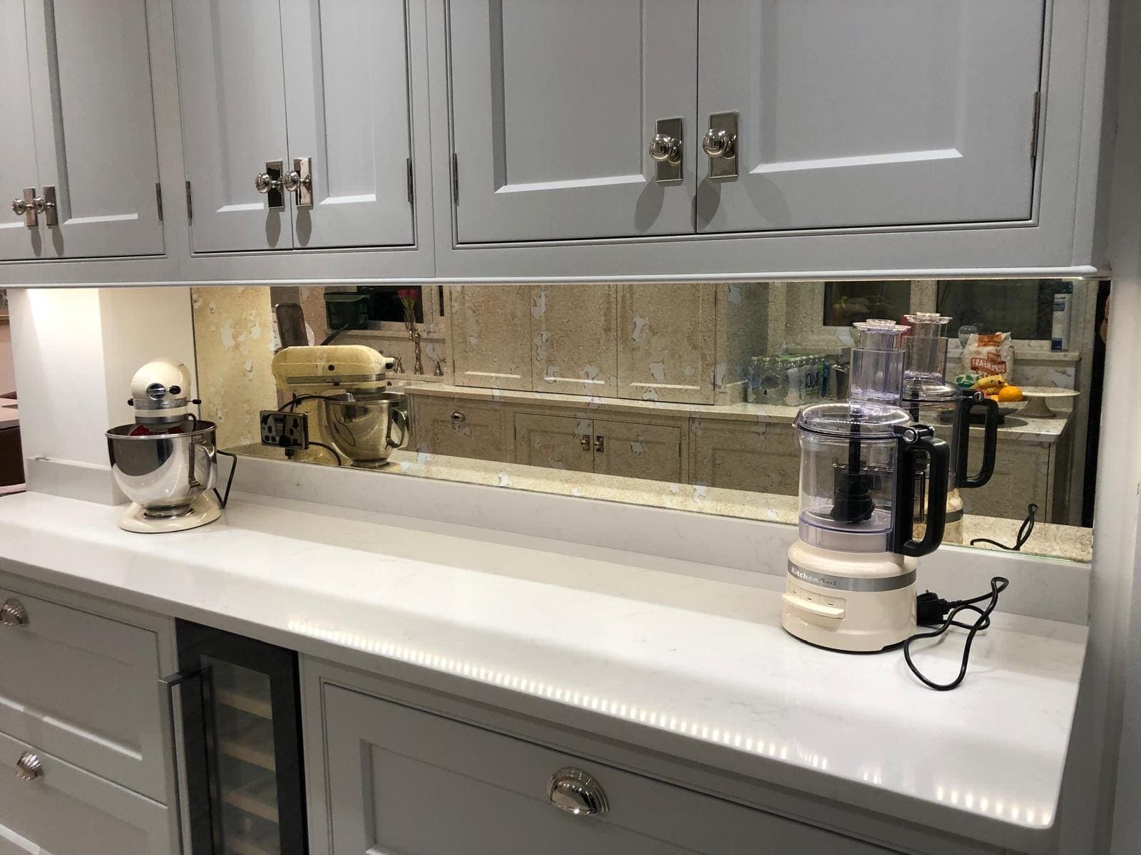 Antique mirror splashback between grey wall cabinets and a white quartz worktop