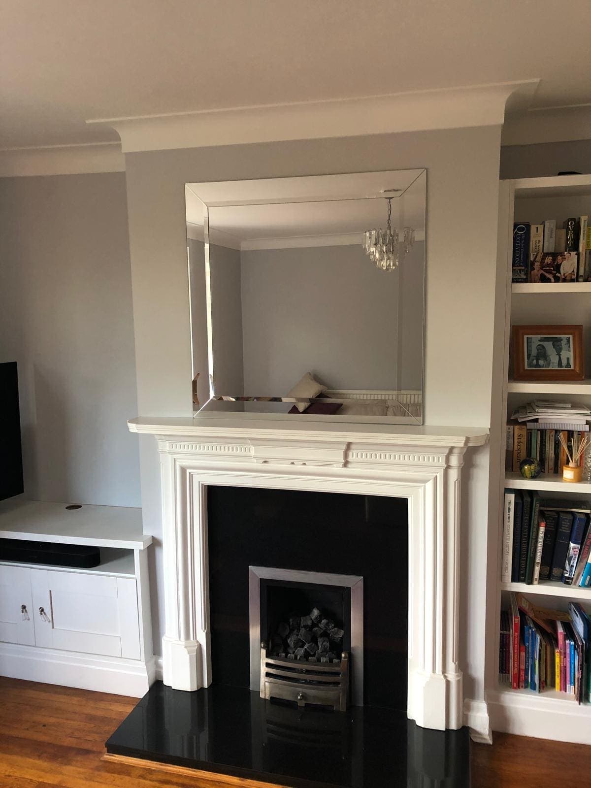 Bevelled mirror above a white fireplace with a black hearth