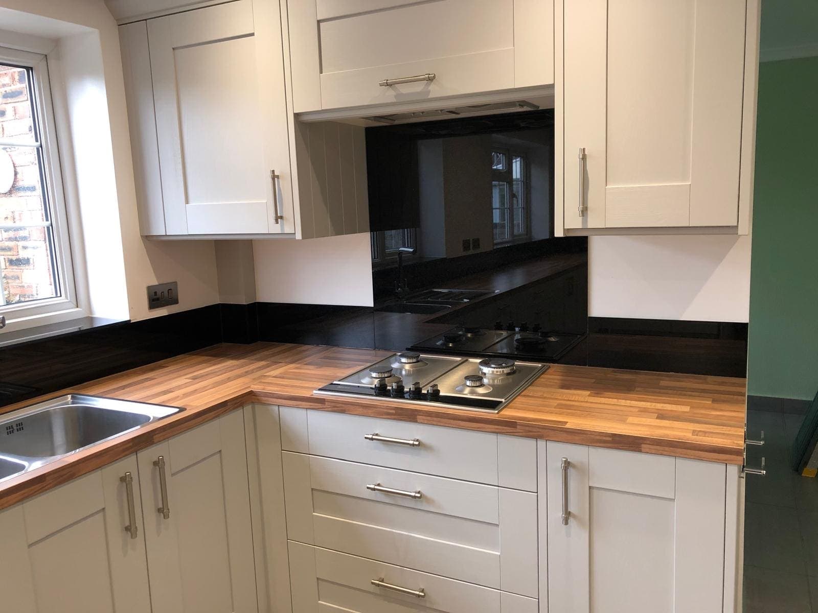 Black glass splashback behind a gas hob in a cream shaker kitchen with wood worktops