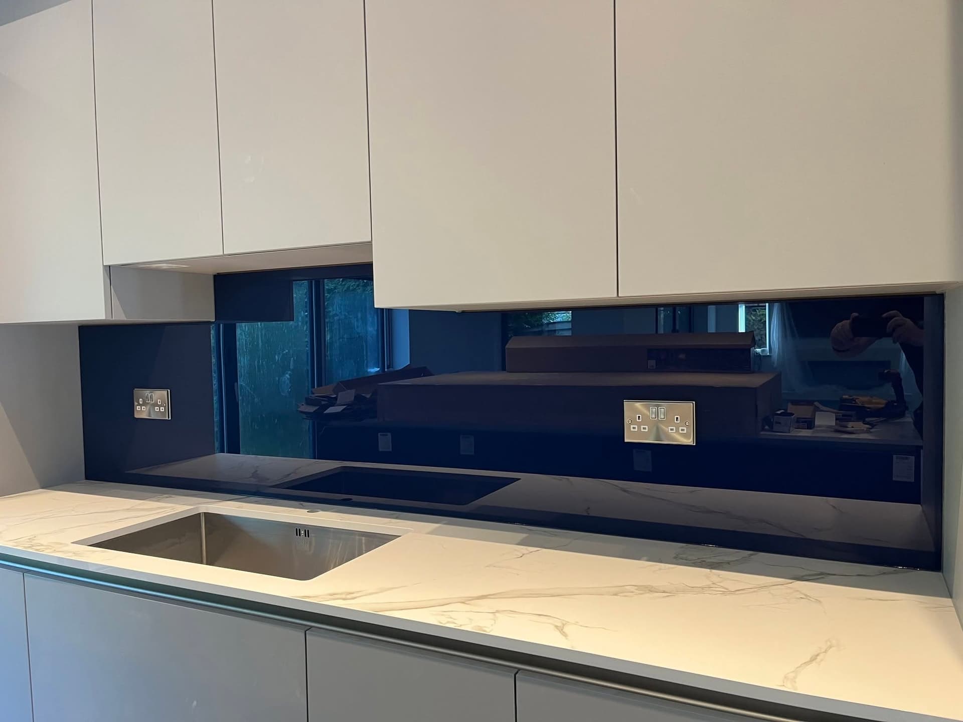 Black glass splashback in a white handleless kitchen with a marble-effect worktop