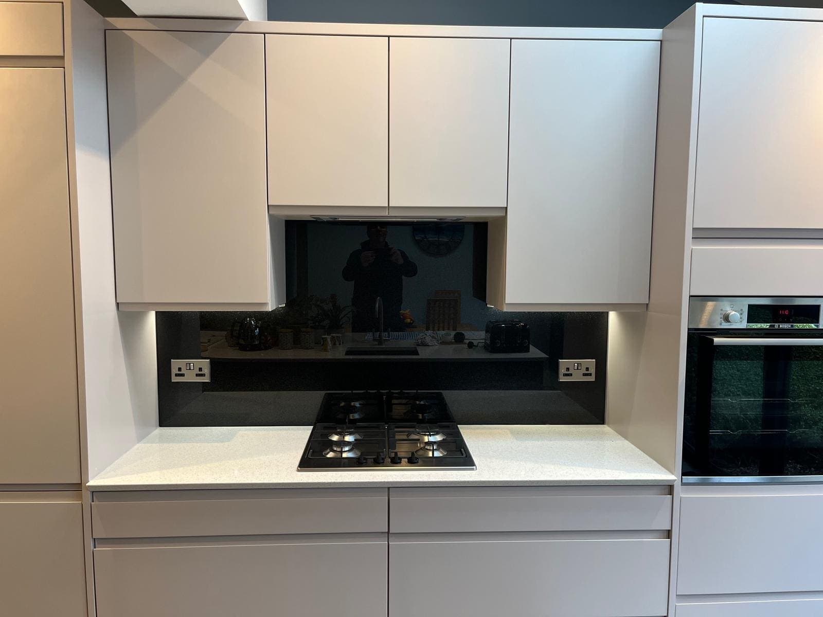 Black glass splashback between white wall units behind a gas hob