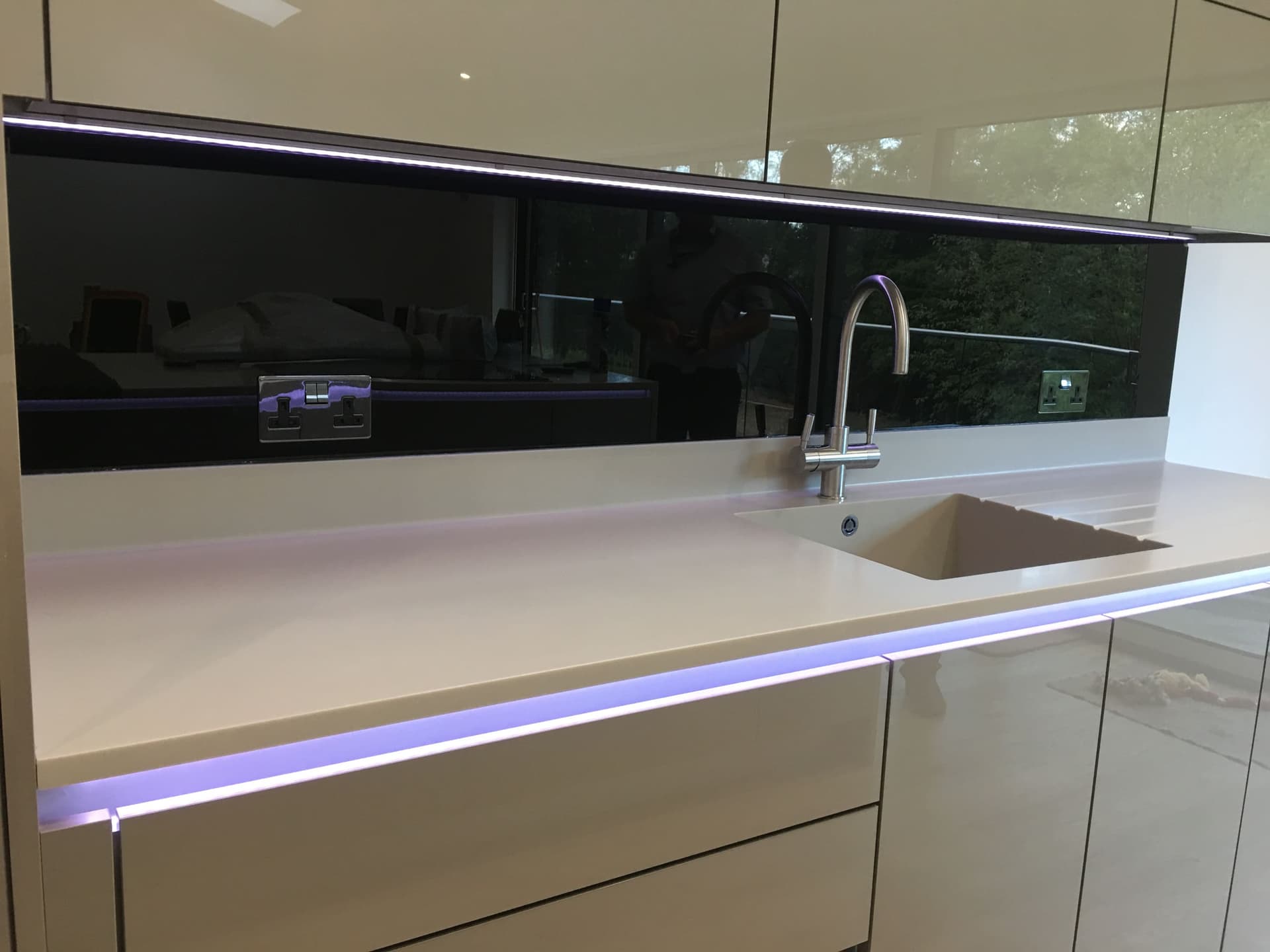Black glass splashback above a white worktop with LED plinth lighting
