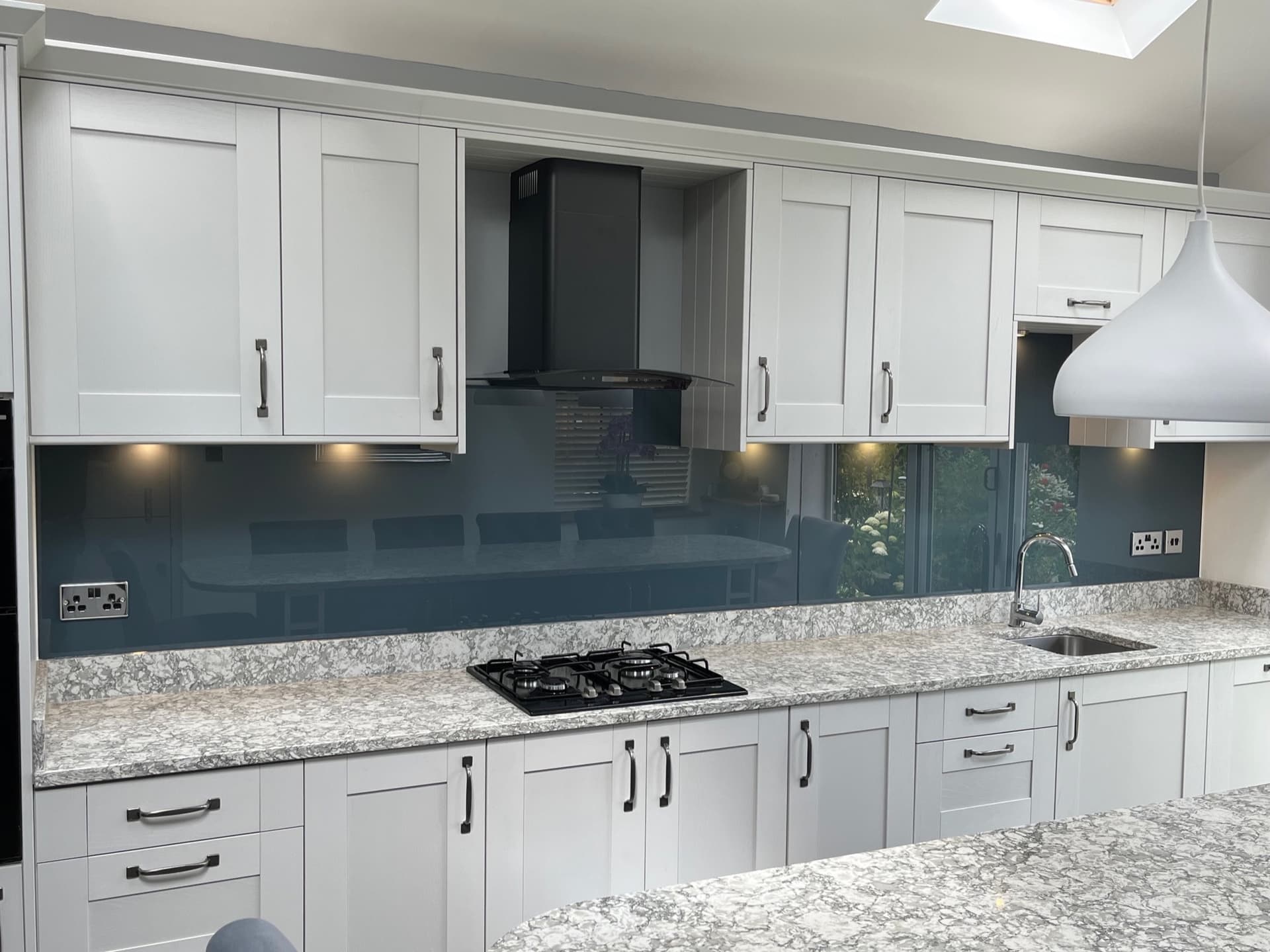 Blue-grey glass splashback in a white shaker kitchen with granite worktops