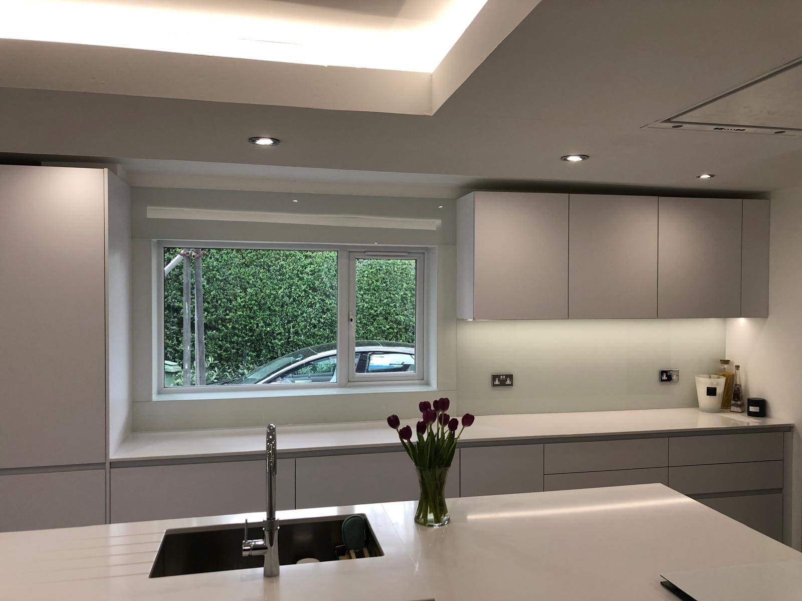 Cream glass splashback around a kitchen window in a grey handleless kitchen