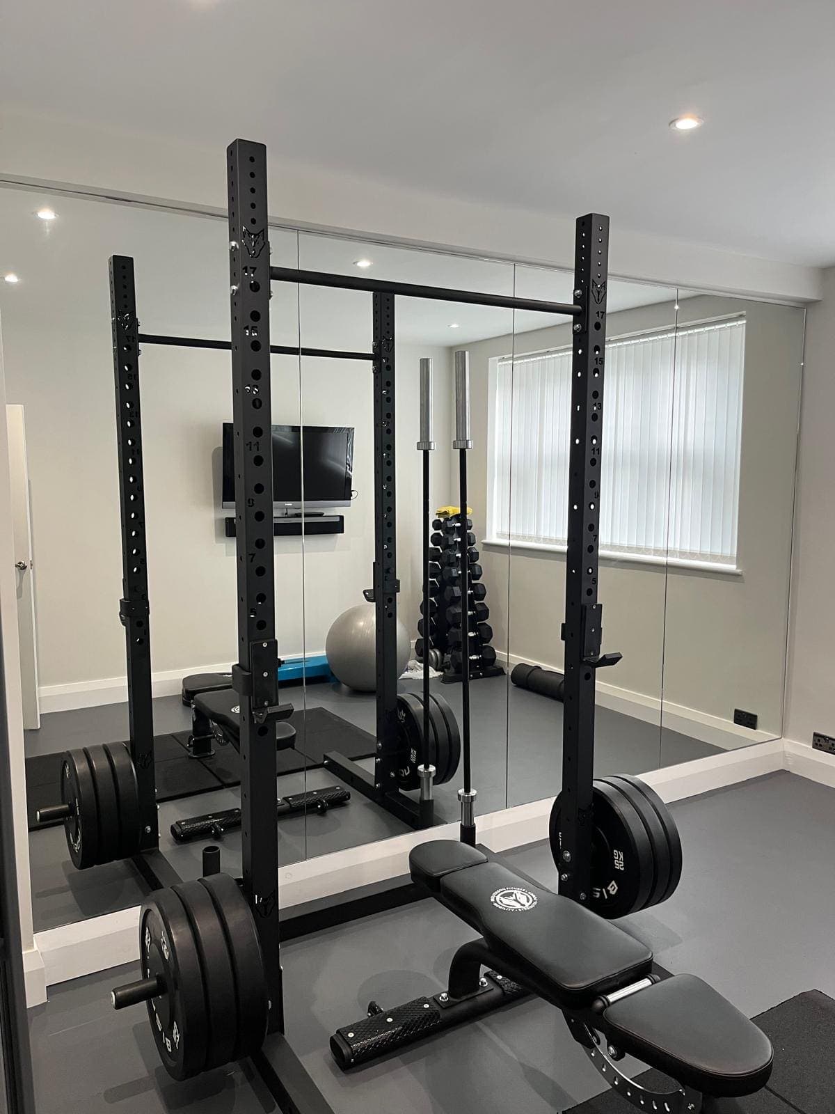 Floor-to-ceiling mirror wall behind a squat rack in a home gym