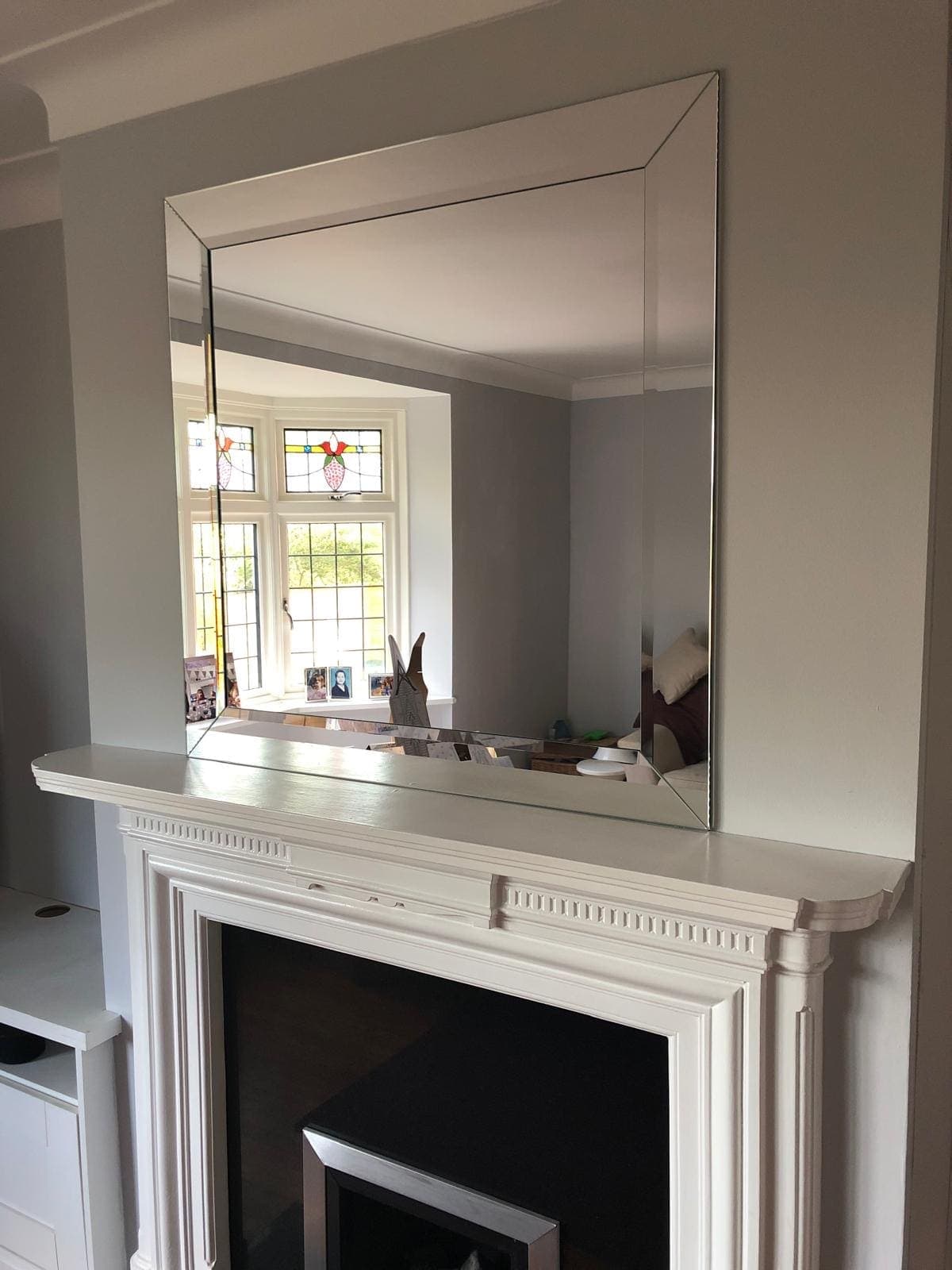 Large bevelled mirror above a white fireplace mantel