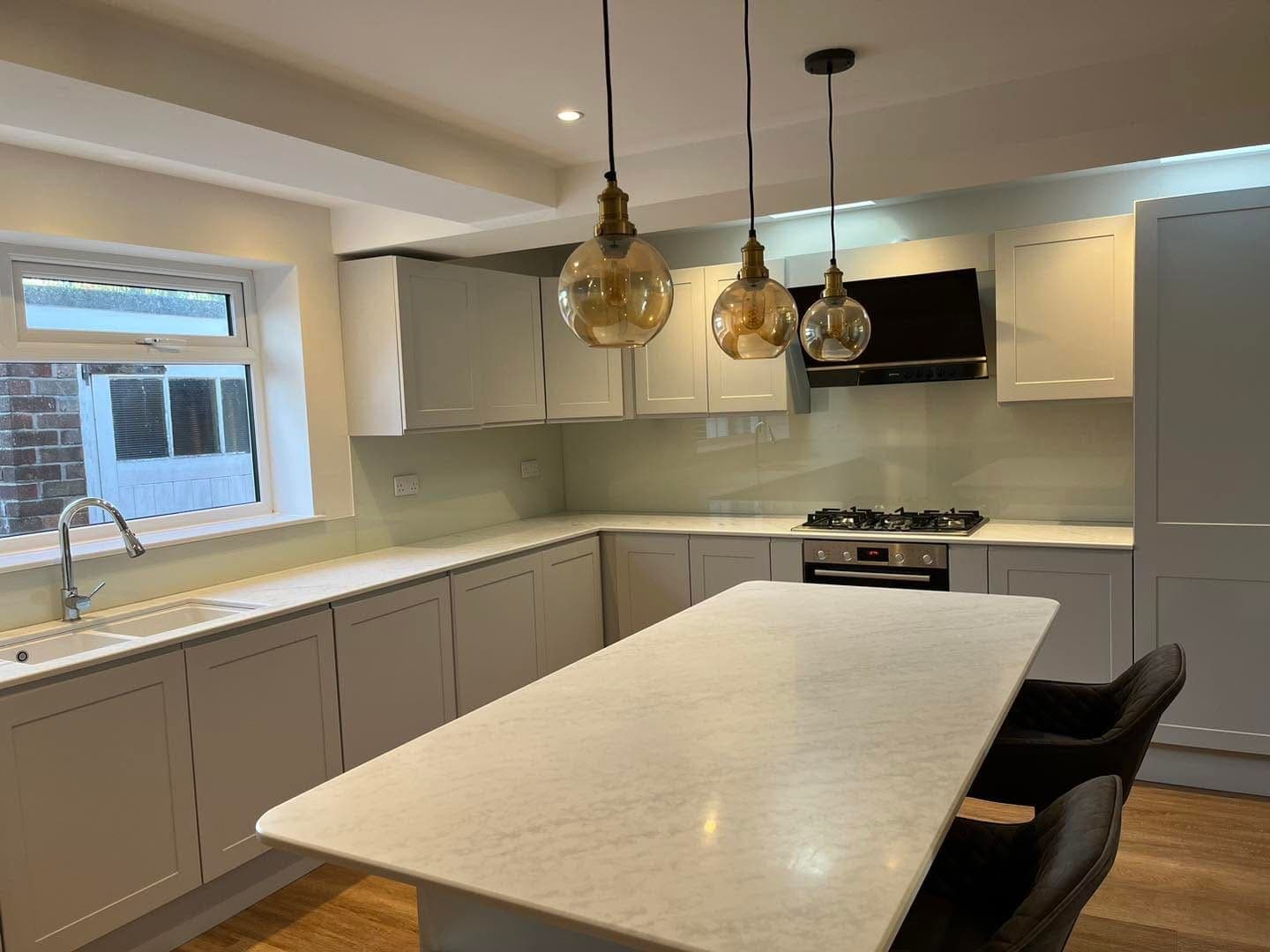 Pale green glass splashback running the length of an L-shaped grey shaker kitchen