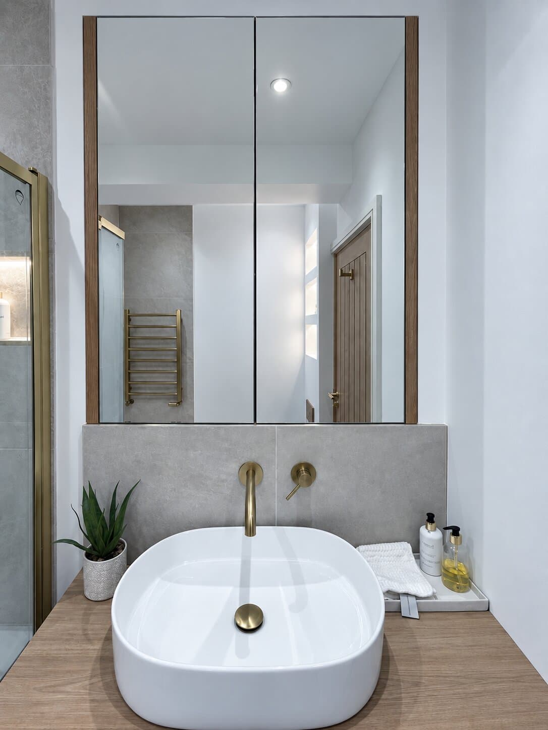Tall two-door mirror cabinet above a bathroom basin with brass taps